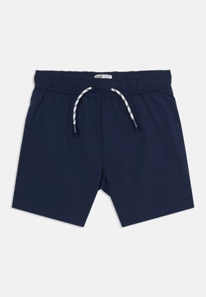 Laivastonsiniset shortsit, joissa on joustava vyötärönauha ja valkoinen, mustaraidallinen nyöri, aseteltuna tasaisesti valkoiselle taustalle.