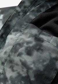 Textúrovaná tkanina v čierno-bielej farbe s bodkovaným vzorom. Mäkký čierny materiál kontrastuje s vzorovaným povrchom, čím zobrazuje hĺbku a detail.
