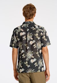 Camicia nera a maniche corte con motivo floreale tropicale, dotata di colletto a scollo e realizzata in tessuto leggero e texture.