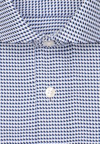 Camicia con bottoni con un motivo a scacchi blu e bianchi, dotata di un bottone in plastica bianca semplice e di un colletto. Texture liscia.