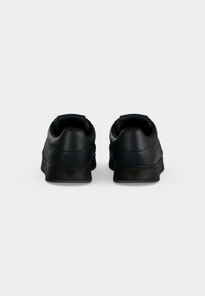 Paire de baskets en cuir noir vues de dos avec un logo subtil sur le talon, sur un fond uni gris clair.