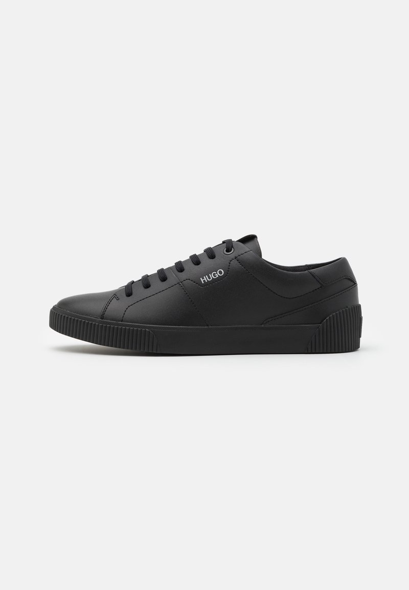 Baskets basses noires avec lacets noirs, semelle texturée et logo "HUGO" sur le côté, présentées en profil latéral sur un fond uni.