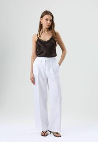 Black satin camisole with lace trim paired with white linen wide-leg trousers featuring a belted waist and gold-tone buttons. Black heeled sandals.