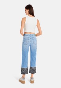 Light blue cropped jeans with leopard print cuffs and back pockets, paired with a white sleeveless top and light-colored shoes.