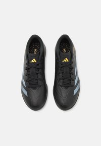 Pari kenkäedistä mustia Adidas Predator -jalkapallokenkiä sinisillä raidoilla ja keltaisella logolla, kuvattuna ylhäältäpäin valkoista taustaa vasten.