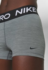Gray athletic shorts with a textured fabric, featuring a black waistband with "NIKE" in white lettering and a small black logo on the leg.