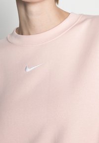 Ljusrosa sweatshirt med rund halsringning, tillverkad av mjukt material. Har en liten vit broderad Nike-logga på bröstet.