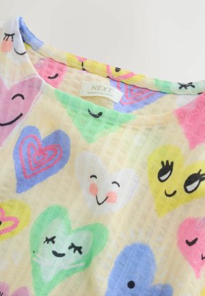 Bavlněné tričko s kulatým výstřihem, zdobené barevnými motivy srdcí v růžové, zelené, modré a žluté na světle žlutém pozadí.