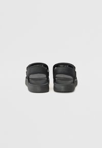 Svarta sandaler med två justerbara remmar, en mjuk gummisul, och en minimalistisk design. Bakifrån framhävs den mjuka texturen.