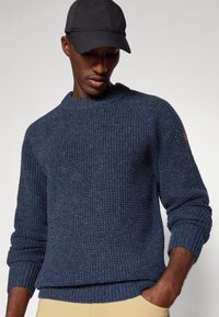 Granatowy sweter dzianinowy o ribbowanej strukturze, z okrągłym dekoltem i mankietami. Posiada wyraźny szew na ramieniu oraz subtellne oznakowanie.