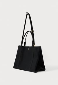 Μαύρη ορθογώνια τσάντα ώμου με δύο χερούλια και μία ρυθμιζόμενη άποψη, που διαθέτει ένα μικρό χρυσό κουμπί μπροστά.