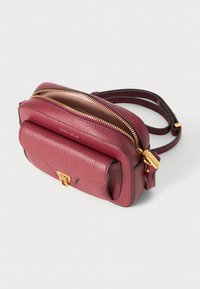 Burgundy leather crossbody bag with gold hardware, double zipper, and a front pocket. Textured finish with adjustable strap. Compact design.