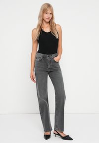 Un body noir et un jean gris taille haute à jambes droites. Le denim présente un lavage délavé avec des poches avant et des coutures subtiles. Des talons aiguilles noirs.