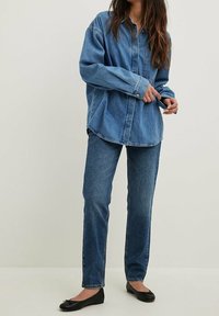 Outfit in denim con camicia e jeans di blu medio. La camicia presenta un colletto con bottoni e una tasca; i jeans sono a gamba dritta con una vestibilità classica.