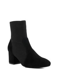 Bottine en suède noir avec un talon bloc et un bout arrondi, dotée de détails de panneaux cousus sur le dessus.