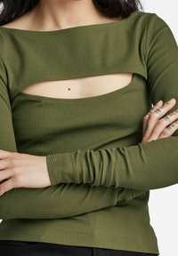 Oliwkowa, prążkowana bluzka z długim rękawem z szerokim dekoltem i wycięciem na klatce piersiowej. Dopasowane rękawy z marszczonym wykończeniem na nadgarstkach.