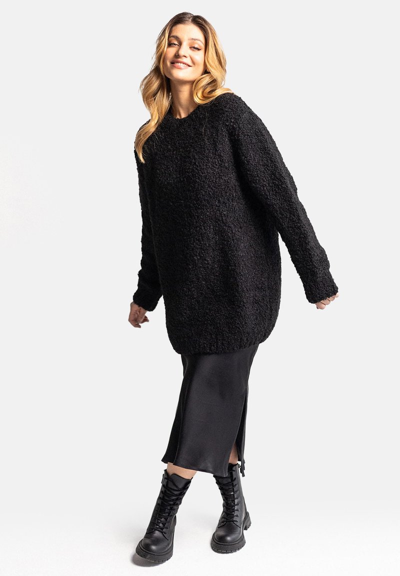 Czarny, oversizowy sweter z teksturowanej tkaniny, z długimi rękawami i okrągłym dekoltem. W połączeniu z jedwabną czarną spódnicą i butami wojskowymi.