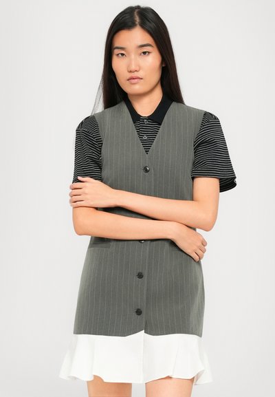 Giovane donna con lunghi capelli scuri che indossa una polo a righe bianche e nere e un vestito grigio a righe con orlo bianco a volant.