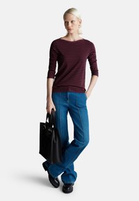 Bordowy i granatowy pasiasty top z długim rękawem, niebieskie dżinsy w stylu dzwonów z białymi szwami, czarna torebka, czarne buty na platformie. Gładka tekstura materiału.