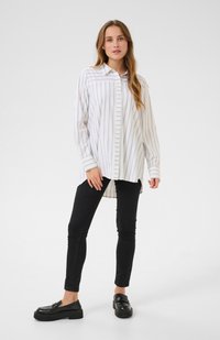 White button-up shirt with light gray vertical stripes, long sleeves, and a curved hem, paired with black skinny jeans and black loafers.