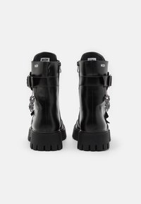 Stivali ankle in pelle nera con suola spessa, chiusura con zip e dettagli decorativi a catena sul retro. Design minimalista con logo.