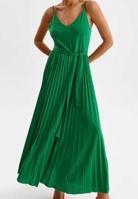 Grön plisserad maxiklänning med spaghettiband, v-ringning och knytskärp i midjan. Tillverkad av lättviktigt tyg med slät textur.