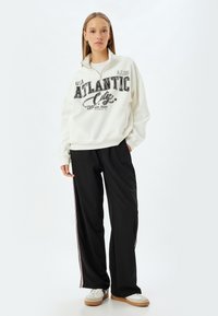 Sudadera de felpa blanca con gráfico de "Atlantic City", cuello alto y puños acanalados, combinada con pantalones de chándal negros con rayas laterales.