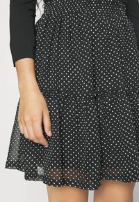 Černé šaty s puntíky a vrstvenou, lehkou sukní. Vrchní část má elastickou výšivku a látka vypadá lehce a průhledně.