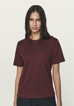 Bordeaux korte mouwen t-shirt in een zachte, gladde katoenstof met een klassiek ronde hals en een comfortabele pasvorm, gecombineerd met zwarte broek.