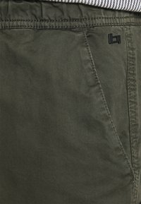 Olive green cotton shorts with a smooth texture, featuring a side pocket and a small black logo accent.