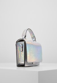 Metalisk sølvhåndtaske med en tekstureret, præget overflade, der har et kort håndtag og en magnetisk flaplukning.