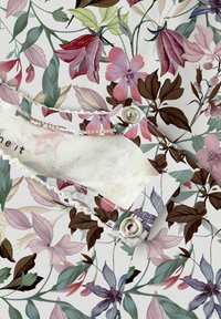 Bloemmotiefstof in pastelkleuren, met roze en groene bladeren. Bevat een witte scalloped rand en knoopdetail op een kraag.