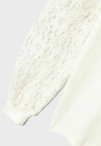 Top blanco con mangas de encaje floral y cuerpo acanalado. Las mangas son transparentes con una apariencia texturizada, y los puños son sólidos.