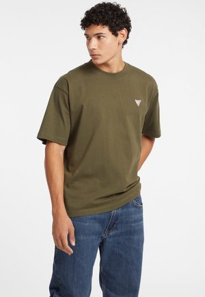 Oliven grøn t-shirt i cotton med korte ærmer, rund hals og et lille trekantet logo på venstre bryst. Båret sammen med blå denim jeans.