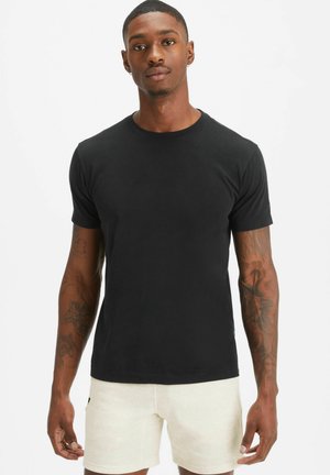 Black cotton t-shirt with short sleeves, crew neckline, and a classic fit; smooth texture; worn with light-colored shorts.