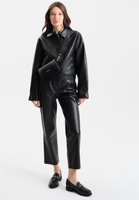 Zwarte leren cropped jack, nauwsluitende broek en zwarte loafers. Krokodillen-embossed crossbody tas met gouden hardwareaccenten. Soepele textuur.