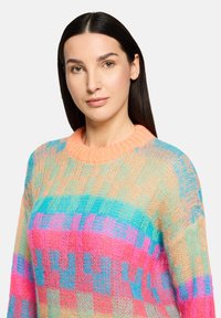 Pull tricoté coloré présentant un motif à mailles ouvertes, avec des rayures horizontales en rose, bleu et orange. Col rond et coupe ample.