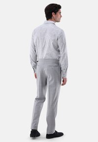 Camicia a maniche lunghe grigia chiara a motivo, abbinata a pantaloni grigi chiari su misura con tasche posteriori e linguette laterali regolabili.