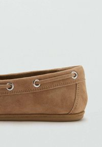 Braune Wildleder-Mokassin-Schuhe im Stil mit Metallösen und Schnürdetails entlang der oberen Kante, flache Sohle und sichtbare Nähte.