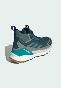 Grüne und graue Sportschuhe mit einer strukturierten Oberseite, kontrastierenden türkisfarbenen Akzenten, reflektierenden Details und einer dicken weißen Sohle.