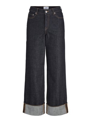 Tumšas džinses ar platām kājām, augstām jostasvītnēm, sarullētām maliņām ar kontrastējošu zilu audumu un oranžām šuvēm.