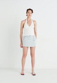 Bijela halter vratna majica i mini suknja s plavim prugama i bočnim dugmadima. Model nosi sandale s prozirnim petama, uz minimalne dodatke.