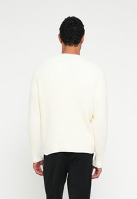 Kermansävyinen vohvelineulottu rento neuletakki, jossa on resorit hihansuissa ja helmassa sekä pyöreä taka-kaula-aukko. Yhdistetty mustiin housuihin.