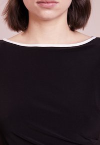 Svart topp med bred halsringning och vit kantning, slät textur och figursydd silhuett som framhäver en enkel men modern design.