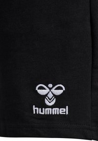 Svarta idrottsshorts i strukturerad väv, med en framträdande vit broderad logotyp med geometrisk design i nedre vänstra hörnet.