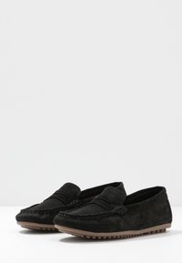 Black suede loafers with a stitched design, flat rubber sole, and a smooth texture. Features a decorative band across the front.