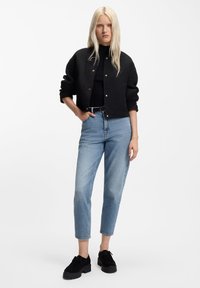 Melnā teksturētā bombardieru jaka, pieguloša melna topiņa, gaiši zili augsto jostasvietu džinsi un melni platformas apavi. Jakai zelta pogas.