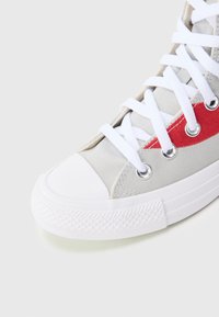 Γκρι καμβαδένιο ψηλό αθλητικό παπούτσι με λευκή λαστιχένια μύτη, λευκά κορδόνια, ασημένιες τρύπες και κόκκινο πλαϊνό σχέδιο. Υφή στη σόλα για καλύτερο κράτημα.