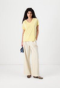 V-neck yellow top paired with loose, cream-colored trousers. Accessories include a small blue bag and leopard print flats.