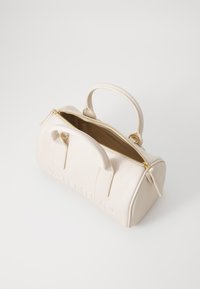 Beige leather handbag with a rounded shape, gold zipper, top handle, and embossed logo on the front. Interior is visible and unlined.